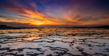 Okyanusun üzerinde güzel bir gün batımı kayalık plajlar ve ön planda gelgit havuzları.