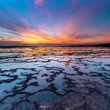 Okyanusun üzerinde güzel bir gün batımı kayalık plajlar ve ön planda gelgit havuzları.