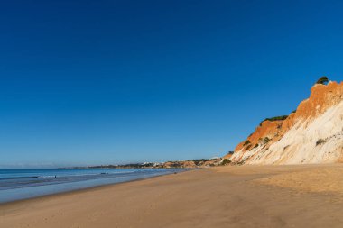 Güneşli bir günde renkli kum kayalıkları olan geniş, boş bir kumsal manzarası.