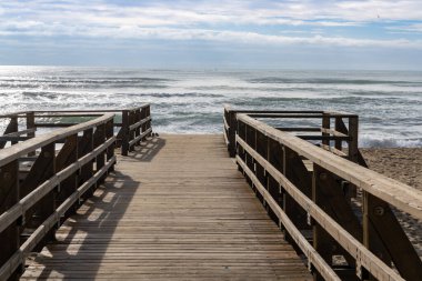 Tahta bir sahil yolu ve sahil girişi fırtınalı dalgalar ve gökyüzüyle doğrudan sahile çıkar.