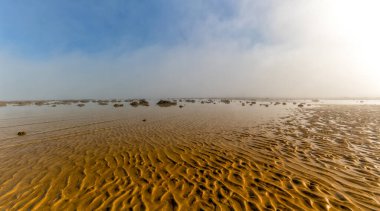A panorama landscape of fog lifting over an endless wadden sea beach at low tide clipart