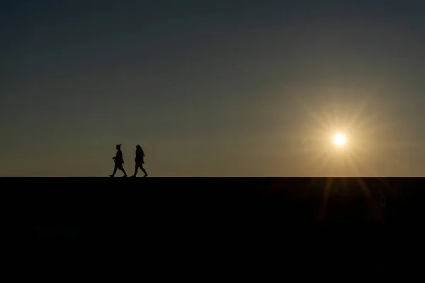 Silhueta Duas Mulheres Andando Uma Parede Com Pôr Sol Céu — Fotografia de Stock