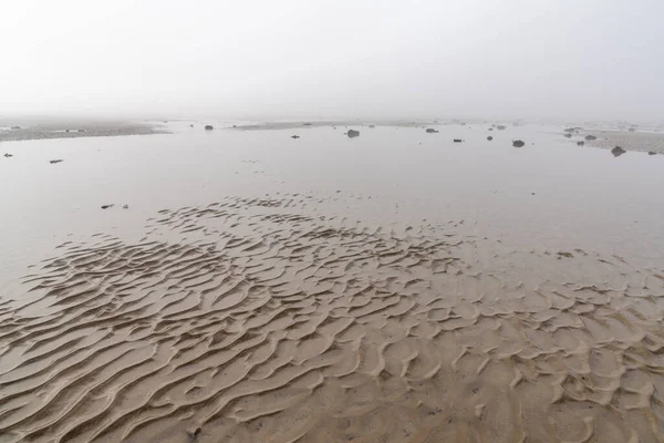青い空に霧を持ち上げながら砂の構造物や岩や潮溜まりと干潮時に発見された無限の海床 — ストック写真