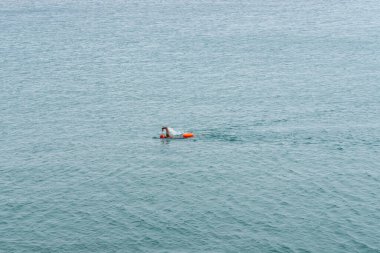 Turuncu şapkalı ve kuru çantalı uzun mesafeli bir yüzücü sonsuz açık okyanus suyunda yüzüyor.