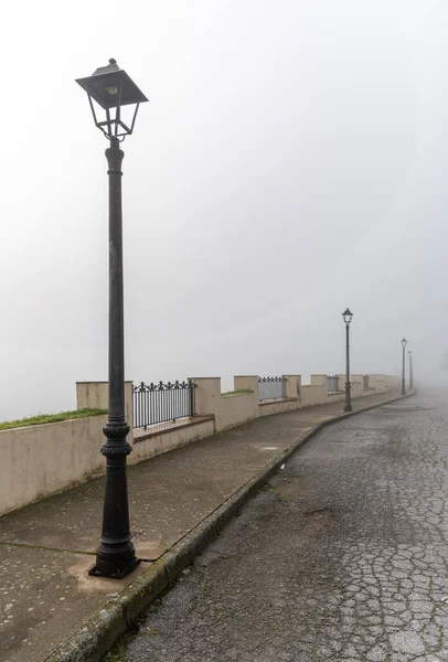 An urban street in the daytime with very thick fog and mist and a row of nostalgic old black street lamps