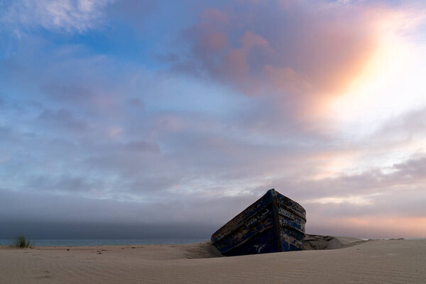красочные обломки старой деревянной лодки, похороненной в песке с красивым закатом неба и океана позади