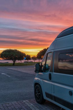 Sahil otoparkında, gün batımının altında park etmiş bir karavanın yakın görüntüsü.