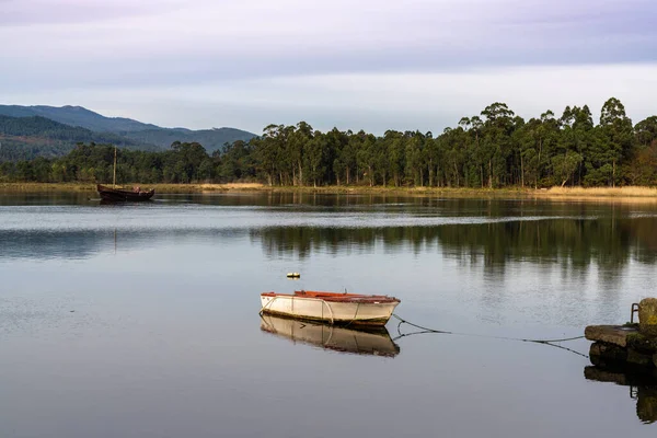 Two boats anchored on a calm and peaceful river with hills and mountains and forest behind