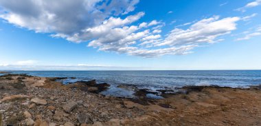 Kayalık bir Akdeniz sahili manzarası. Dalgalar alçak, anlamlı bir gökyüzü altında.