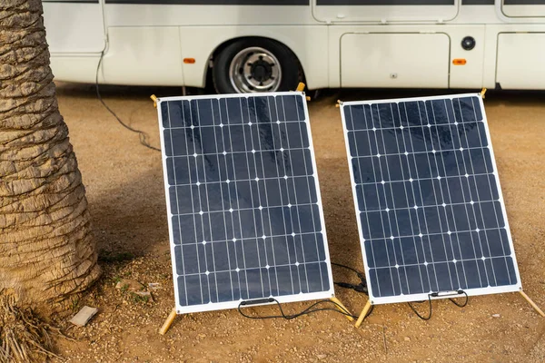 Two mobile solar panels next to a palm tree with a large RV motor home behind