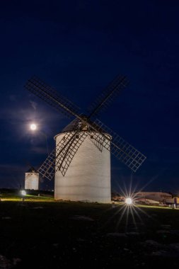La Mancha 'nın tarihi beyaz yel değirmenlerinin gece vakti Campo de Criptana kasabasının üzerindeki dolunay altında görüntüsü.