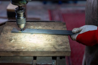 Bir metal işçisi, bir bank matkabıyla metali deliyor.