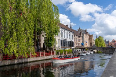 Bruges, Belçika - 12 Mayıs 2021: turistler tarihi Bruges şehir merkezindeki kanallarda huzurlu bir tekne turunun keyfini çıkarıyorlar.