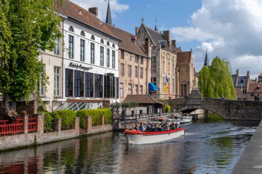 Bruges, Belçika - 12 Mayıs 2021: turistler tarihi Bruges şehir merkezindeki kanallarda huzurlu bir tekne turunun keyfini çıkarıyorlar.