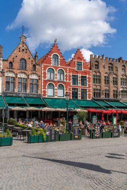 Bruges, Belçika - 12 Mayıs 2021: İnsanlar Brüksel 'deki Pazar Meydanı' ndaki restoranlarda, arka planda birçok tarihi tuğla bina bulunan bir günün tadını çıkarıyorlar.