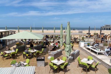 Scheveningen, Hollanda - 16 Mayıs 2021: İnsanlar Lahey yakınlarındaki deniz kıyısındaki Scheveningen tatil beldesindeki restoranlardan birinde yemek yiyip içki içiyorlar
