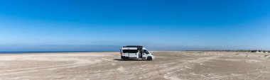 Ringby, Danimarka: 31 Mayıs 2021: Uçsuz bucaksız beyaz bir kumsalda, okyanusun arkasında park etmiş gri bir karavan panoraması
