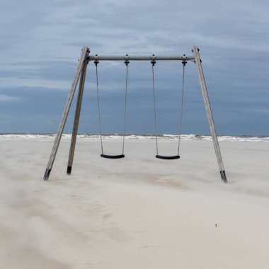 Kuzey Almanya 'nın Wadden Denizi' nin arka planında boş bir kumsalda iki salıncak.