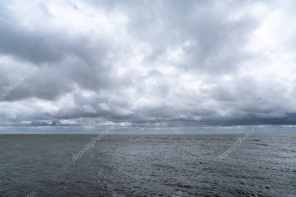 Landscape of expressive cloudy and overcast sky over a windbeaten Wadden Sea in the Netherlands