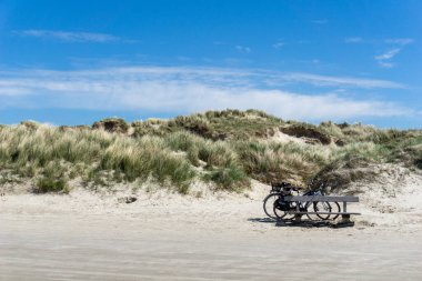 two bicycles parked in front of a large sand dune covered in grasses and reeds under a blue sky clipart