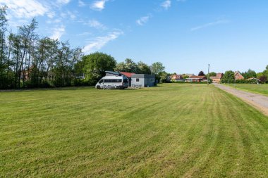 Flauenskjold, Danimarka - 4 Haziran 2021: Yeşil arazili geniş bir karavan parkı ve sağlık tesisleri binasının yanına park edilmiş gri bir karavan.