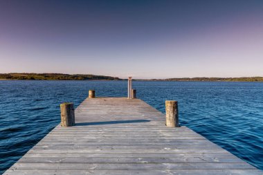 Bir fiyortun koyu mavi sularına çıkan ahşap bir tahta kaldırım. Alacakaranlık eflatun bir akşam gökyüzünün altında.