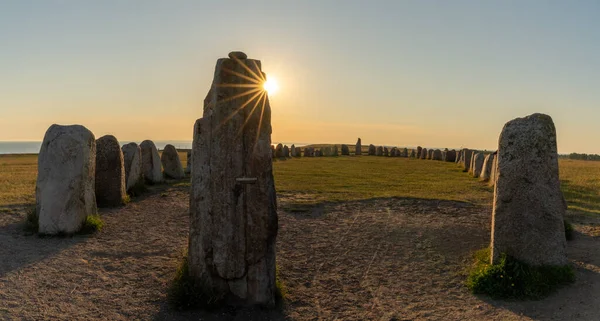 Landscape view of the prehistoric Ales Stenar ship setting on the southern coast of Sweden at sunset with a sun star