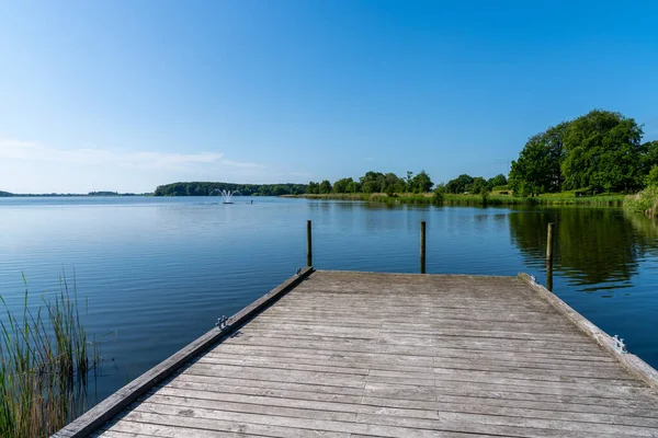 A wooden dock leads out into a calm lake with dark blue water