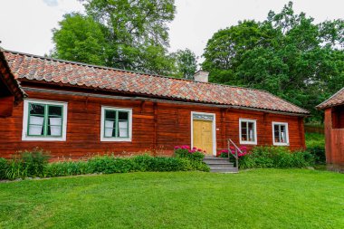 Gamla Uppsala, İsveç - 24 Haziran 2021: Güzel bir yaz gününde yeşil çayırlı İsveç kırsalındaki cennet kırmızısı ev