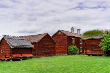 Gamla Uppsala, İsveç - 24 Haziran 2021: Güzel bir yaz gününde yeşil çayırlı İsveç kırsalındaki cennet gibi kırmızı kulübeler