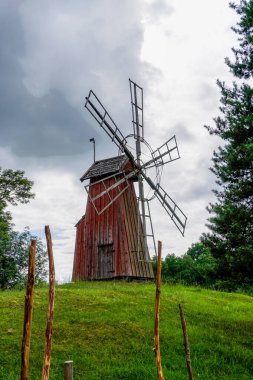 Gamla Uppsala, İsveç - 24 Haziran 2021: Kırsal bölgedeki çimenli bir yel değirmeninin tepesindeki küçük kırmızı ahşap yel değirmeni