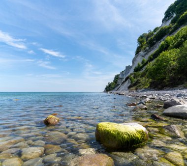 Durgun suları ve beyaz kümülüs bulutlarıyla mavi gökyüzünün altında sarp beyaz tebeşir taşı kayalıkları olan pitoresk bir okyanus ve kıyı şeridi.