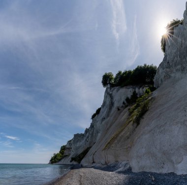 Idyllic yüksek beyaz tebeşir taşı uçurumları ve sakin okyanus suları ve bir güneş yıldızı olan kayalık bir plaj.