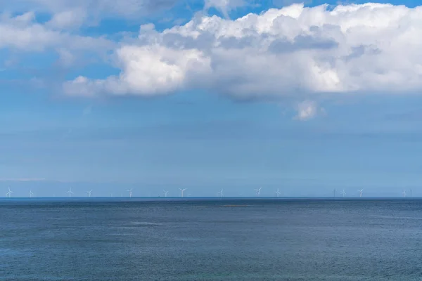 Many wind turbines in the open ocean under a blue sky with white cumulus clouds