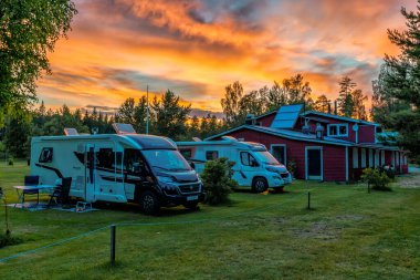 Hallefors, Sweden - 4 July, 2021: beautiful sunset at a Swedish campground in the forest with a red cottage and camper vans in the foreground clipart