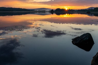 Sakin bir gölün üzerinde renkli bir günbatımı. Suda yansımaları var.