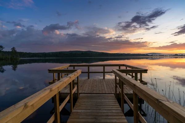 一个木制的码头通向平静的湖面 对岸是一片森林 夕阳西下的天空五彩斑斓 — 图库照片