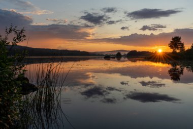 Sakin bir gölün üzerinde renkli bir günbatımı. Suda yansımaları var.