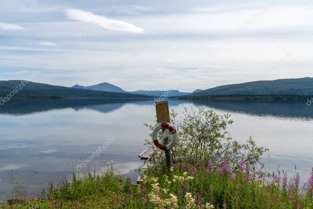 A calm lake with reflections of mountains and sky and a rescue ring in midst of colorful wildflowers in the foreground