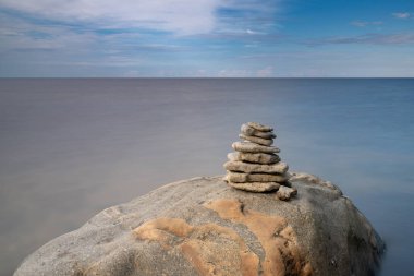 Bir kayanın tepesinde meditasyon yapan bir kaya cairn. Arka planda okyanus ve gökyüzü var.