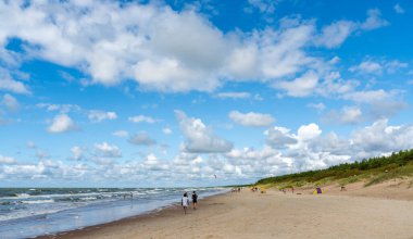 Palanga, Litvanya - 21 Ağustos 2021: İnsanlar sakin okyanusları, yumuşak dalgaları ve kumulları olan sonsuz bir kumsalda yaz gününün tadını çıkarıyorlar.