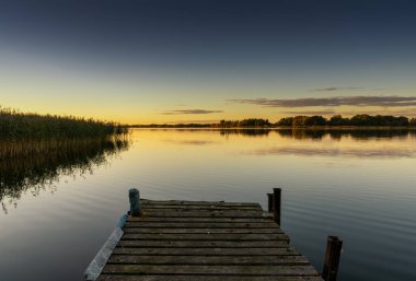 A view of Vilkaviskis Lake in Lithuania at sunset with a wooden dock in the foreground