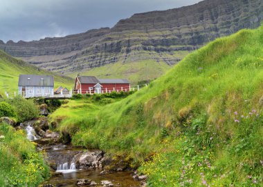 Faroe Adaları 'ndaki Kunoy köyünde bir şelale manzarası ve renkli ahşap evler