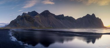 Stokksnes plajının manzarası ve ikonik Vestrahorn 'un ılık sabah ışığında suda yansıması.