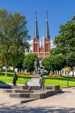 Skien, Norveç - 13 Ağustos 2025: Şehir parkı ve heykelleri olan kırmızı tuğlalı Skien Lutheran Kilisesi manzarası