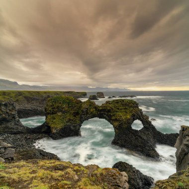 Arnarstapi yakınlarındaki fırtınalı bir yaz sabahında Gatklettur deniz kemeriyle vahşi ve engebeli sahil manzarası.