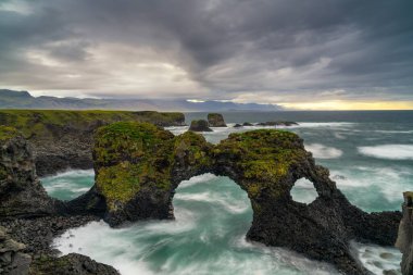 Arnarstapi yakınlarındaki fırtınalı bir yaz sabahında Gatklettur deniz kemeriyle vahşi ve engebeli sahil manzarası.