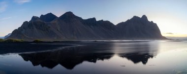 Stokksnes plajının manzarası ve ikonik Vestrahorn 'un ılık sabah ışığında suda yansıması.