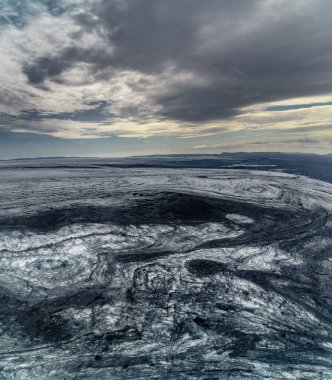 Vatnajokull buzulunun manzarası ve fırtınalı bir gökyüzünün altında siyah kum ve volkanik külle kaplı buz örtüsü.