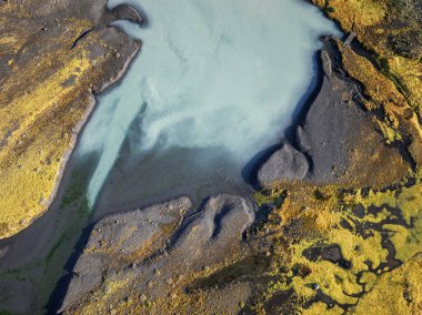 Solheimajokull Buzul Gölü 'nün altındaki nehir yatağı boyunca akan turkuaz buzul erimiş suyun yukarıdan aşağı soyut görüntüsü.
